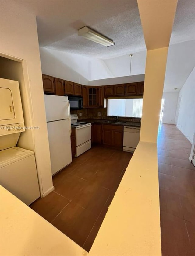 2421 NW 56th Ave Unit 2-202, Lauderhill, FL 33313 - kitchen with white appliances, stacked washer / drying machine, a sink, dark tile patterned floors, and lofted ceiling