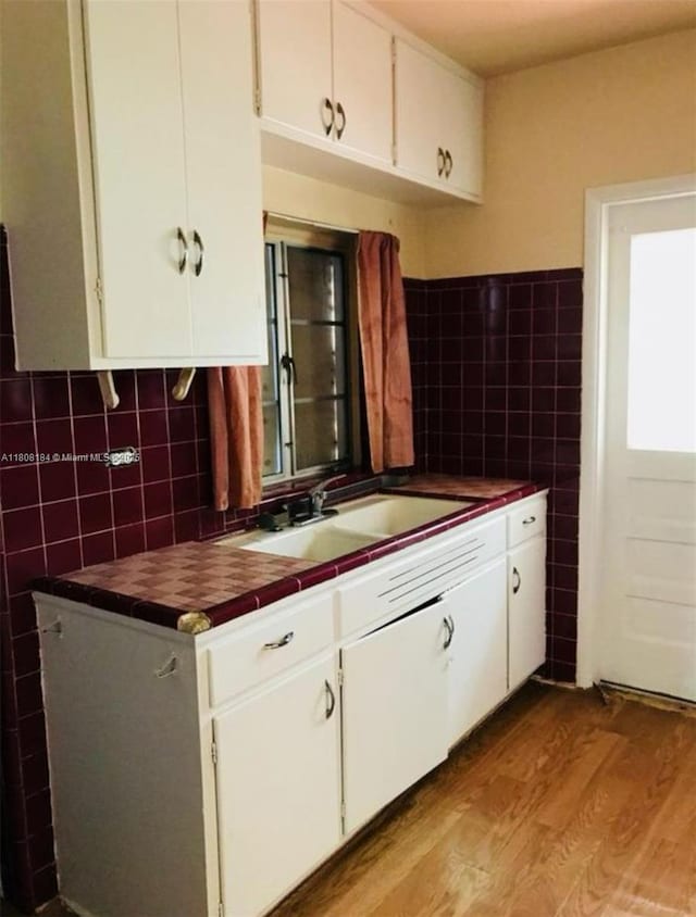 1745 NW 47th St, Miami, FL 33142 - kitchen with tile walls, a sink, white cabinets, and light wood-style floors