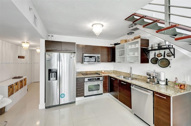 41 SE 5th St Unit 1012, Miami, FL 33131 - kitchen with appliances with stainless steel finishes, a sink, dark brown cabinetry, light stone countertops, and glass insert cabinets