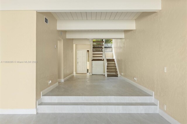 19460 NE 26th Ave Unit 12B, Miami, FL 33180 - stairs with concrete flooring, a textured wall, baseboards, and wood ceiling with exposed beams