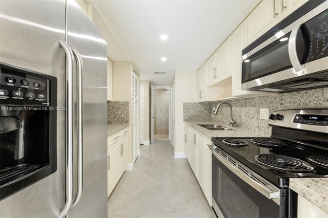 19460 NE 26th Ave Unit 12B, Miami, FL 33180 - kitchen with stainless steel appliances, a sink, backsplash, white cabinetry, and light stone counters