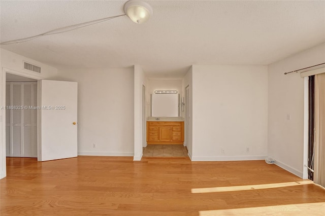 1551 NW 92nd Ave Unit 185, Pembroke Pines, FL 33024 - unfurnished bedroom featuring light wood-type flooring, baseboards, ensuite bathroom, and a textured ceiling