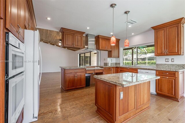 9919 SW 1st Ct, Coral Springs, FL 33071 - kitchen with white appliances, a peninsula, wall chimney exhaust hood, brown cabinetry, and light wood-type flooring