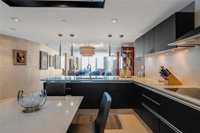 17001 Collins Ave Unit 2501, Sunny Isles Beach, FL 33160 - kitchen featuring dark cabinets, wall chimney exhaust hood, black electric cooktop, a sink, and a peninsula