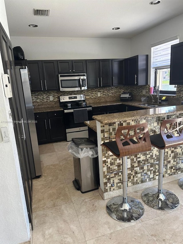 3406 W 88th St, Hialeah, FL 33018 - kitchen featuring stainless steel appliances, dark cabinetry, backsplash, a kitchen bar, and dark countertops