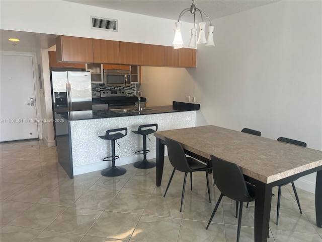 1750 N Bayshore Dr Unit 1410, Miami, FL 33132 - kitchen featuring stainless steel appliances, brown cabinetry, a peninsula, dark countertops, and decorative backsplash