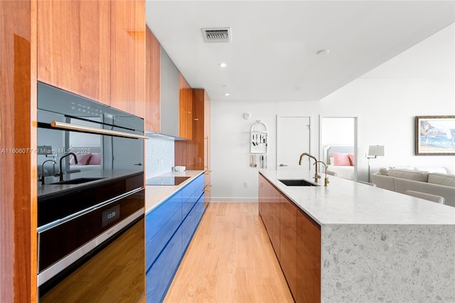 2678 Tigertail Ave Unit 713, Miami, FL 33133 - kitchen with modern cabinets, a sink, light wood-style flooring, an island with sink, and brown cabinetry