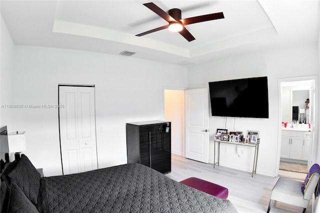 21068 NE 8th Ave, Miami, FL 33179 - bedroom featuring a tray ceiling, light wood-style flooring, connected bathroom, and a ceiling fan
