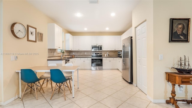 3945 Heron Ridge Ln, Weston, FL 33331 - kitchen with stainless steel appliances, decorative backsplash, white cabinets, a peninsula, and light tile patterned floors
