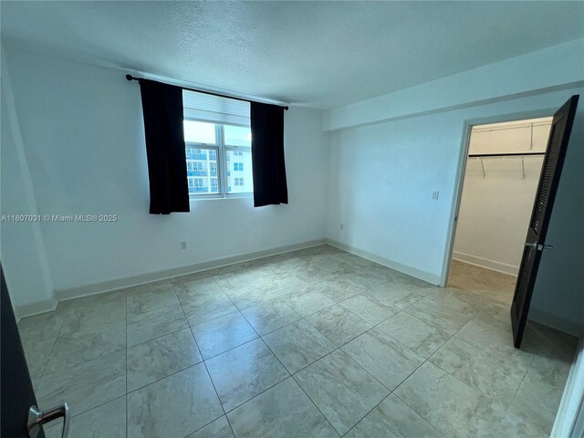7501 E Treasure Dr Unit 9D, North Bay Village, FL 33141 - unfurnished bedroom featuring a textured ceiling, a spacious closet, baseboards, and a closet