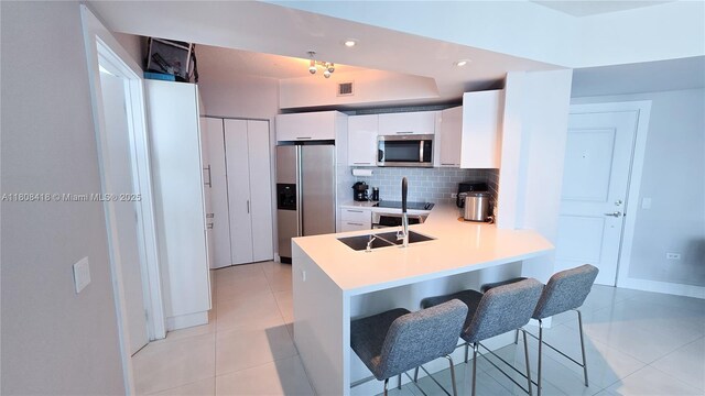 480 NE 30th St Unit 1405, Miami, FL 33137 - kitchen featuring appliances with stainless steel finishes, a peninsula, white cabinetry, a breakfast bar area, and light tile patterned flooring