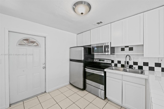 1625 NE 29th St, Pompano Beach, FL 33064 - kitchen featuring appliances with stainless steel finishes, tile counters, a sink, and white cabinets