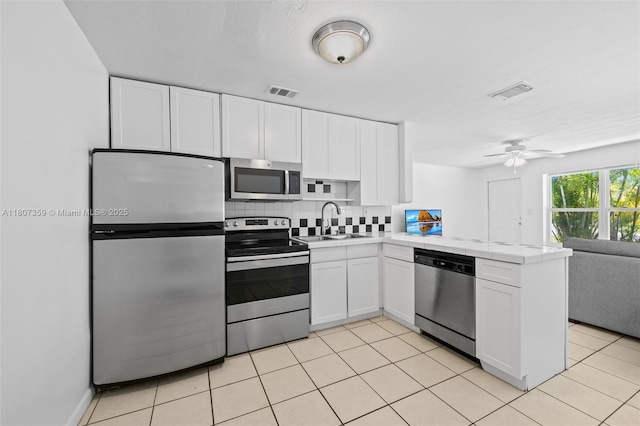 1625 NE 29th St, Pompano Beach, FL 33064 - kitchen with stainless steel appliances, a sink, a peninsula, tile counters, and white cabinetry