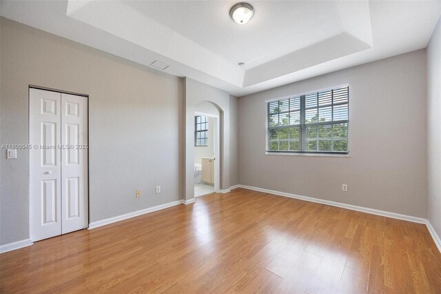 623 NE 21st Ter, Homestead, FL 33033 - unfurnished bedroom with a raised ceiling, light wood finished floors, arched walkways, baseboards, and a closet