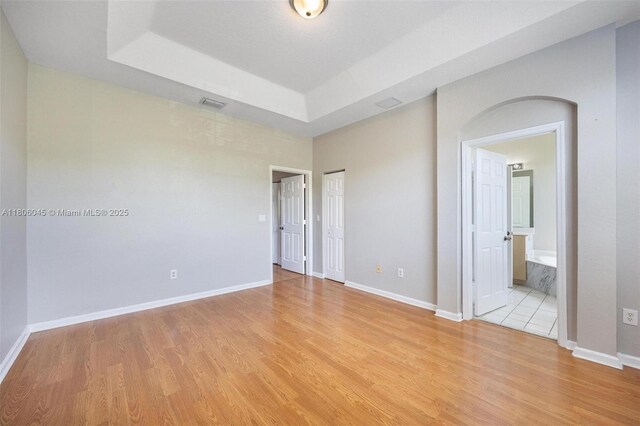 623 NE 21st Ter, Homestead, FL 33033 - unfurnished bedroom with light wood-style floors, a raised ceiling, baseboards, and connected bathroom