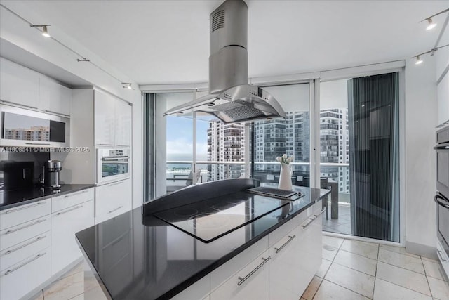 2127 Brickell Ave Unit 2302, Miami, FL 33129 - kitchen with island exhaust hood, dark countertops, modern cabinets, black electric cooktop, and white cabinets