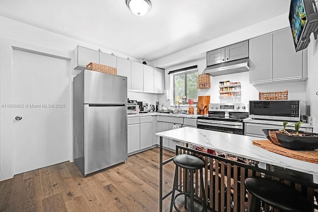 12400 NE 11th Ct, North Miami, FL 33161 - kitchen featuring appliances with stainless steel finishes, light wood-style floors, gray cabinetry, and under cabinet range hood