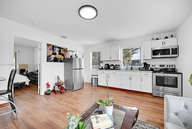12400 NE 11th Ct, North Miami, FL 33161 - kitchen with appliances with stainless steel finishes, light wood finished floors, white cabinetry, and a sink
