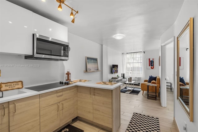710 Washington Ave Unit 323, Miami Beach, FL 33139 - kitchen featuring stainless steel microwave, black electric stovetop, light countertops, a peninsula, and light brown cabinets