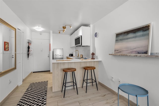 710 Washington Ave Unit 323, Miami Beach, FL 33139 - kitchen with stainless steel microwave, a kitchen breakfast bar, light countertops, white cabinets, and a peninsula