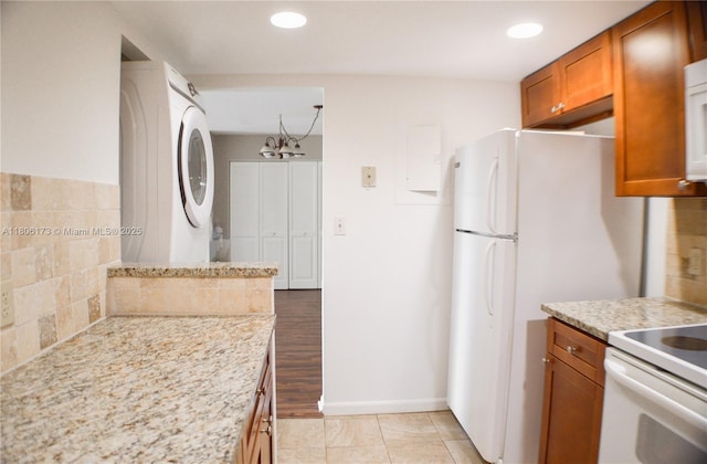 733 SE 1st Way Unit 206, Deerfield Beach, FL 33441 - kitchen featuring stacked washing machine and dryer, brown cabinets, a chandelier, white appliances, and light stone counters
