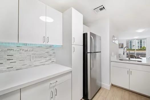 185 SE 14th Ter Unit 1410, Miami, FL 33131 - kitchen with freestanding refrigerator, a sink, light countertops, white cabinetry, and decorative backsplash
