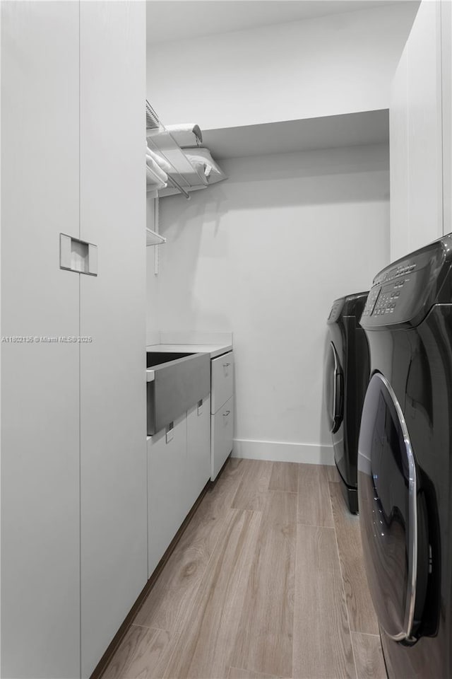 12880 N Bayshore Dr, North Miami, FL 33181 - washroom with washer and clothes dryer, light wood finished floors, baseboards, and cabinet space