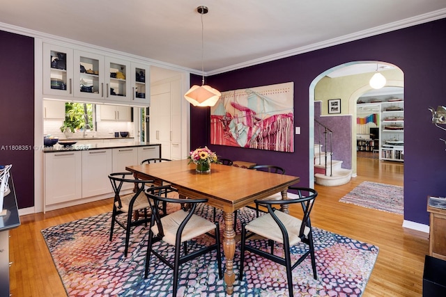 3245 Riviera Dr, Coral Gables, FL 33134 - dining area featuring light wood-style floors, arched walkways, crown molding, stairway, and baseboards