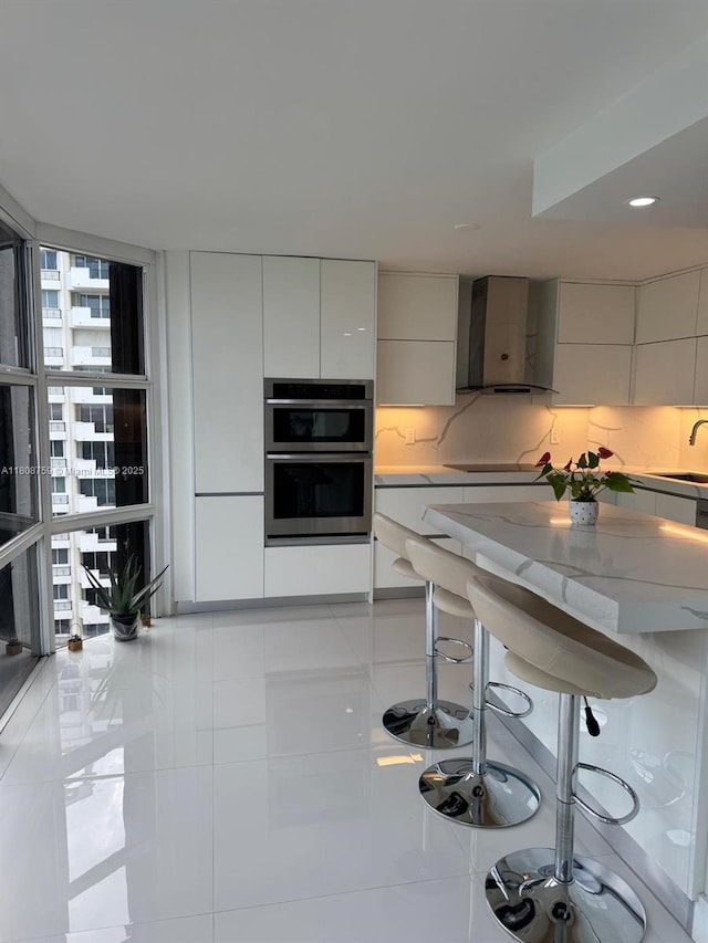 6423 Collins Ave Unit 1001, Miami Beach, FL 33141 - kitchen with modern cabinets, wall chimney range hood, double oven, and light stone counters