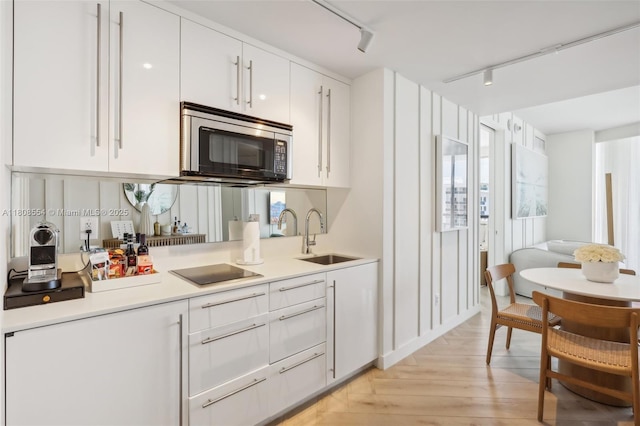 2201 Collins Ave Unit 1511, Miami Beach, FL 33139 - kitchen featuring a sink, stainless steel microwave, rail lighting, black electric cooktop, and white cabinetry