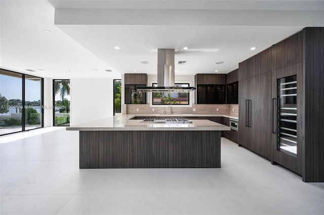 1351 Stillwater Dr, Miami Beach, FL 33141 - kitchen with modern cabinets, decorative backsplash, light countertops, dark brown cabinetry, and island exhaust hood