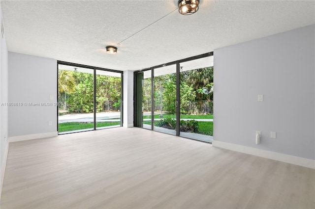 9682 Fontainebleau Blvd Unit 110, Miami, FL 33172 - empty room featuring a wall of windows, wood finished floors, a textured ceiling, and baseboards