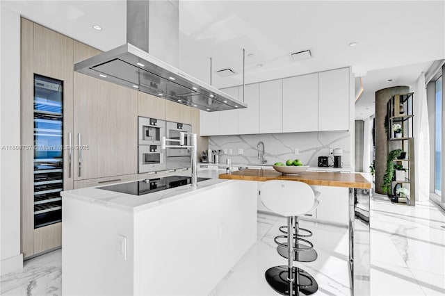 15701 Collins Ave Unit 705, Sunny Isles Beach, FL 33160 - kitchen featuring modern cabinets, island exhaust hood, black electric cooktop, light marble finish flooring, and a sink