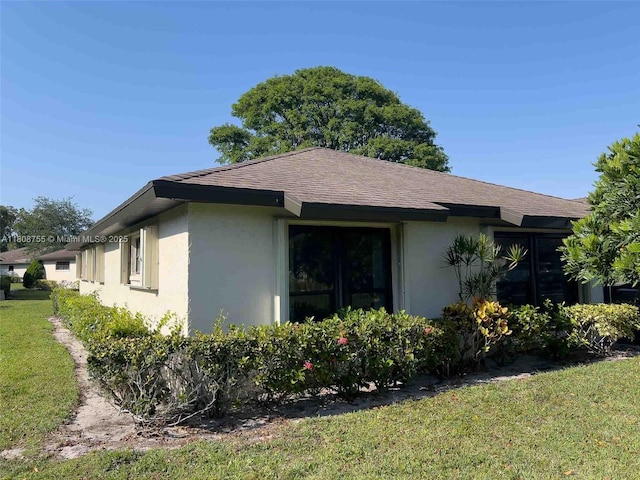 10198 Dovewood Ln Unit A, Boynton Beach, FL 33436 - view of side of home featuring stucco siding, a shingled roof, and a lawn