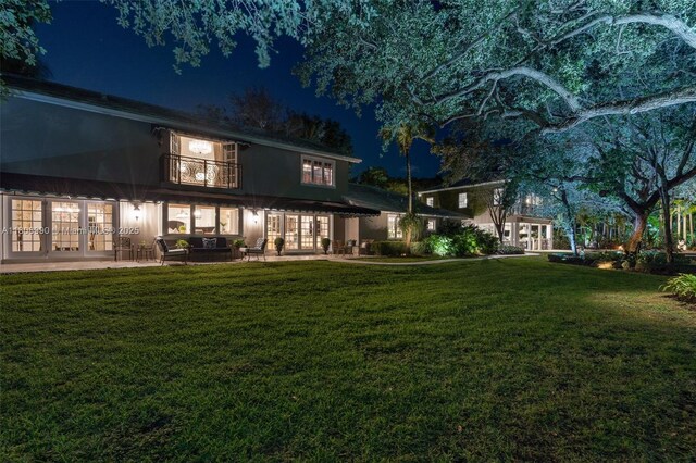 7360 SW 164th St, Palmetto Bay, FL 33157 - back of house at night featuring french doors, a balcony, a lawn, and a patio