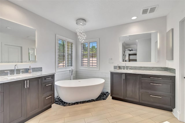 4231 N Magnolia Cir, Delray Beach, FL 33445 - full bathroom featuring two vanities, a freestanding tub, tile walls, and a wainscoted wall