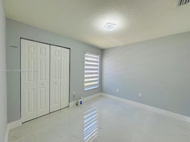 13729 SW 171st Ln, Miami, FL 33177 - unfurnished bedroom with marble look tile flooring, baseboards, a textured ceiling, and a closet