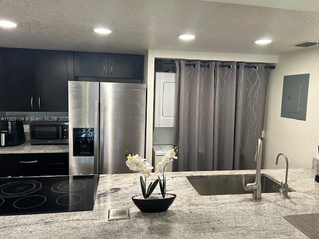 5326 NE 6th Ave Unit E23, Oakland Park, FL 33334 - kitchen featuring stainless steel refrigerator with ice dispenser, black microwave, stacked washing machine and dryer, a sink, and electric panel