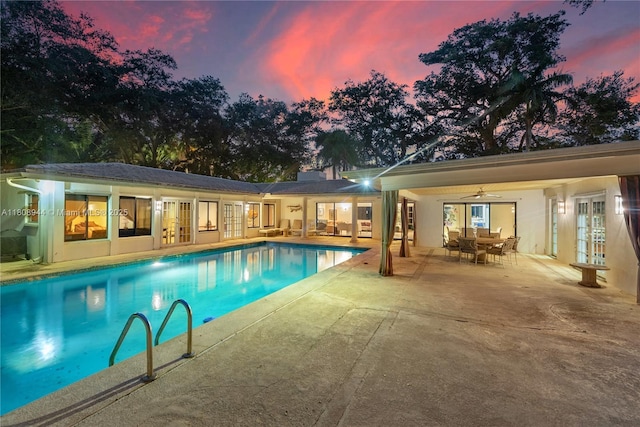 5465 Banyan Trl, Coral Gables, FL 33156 - pool at dusk featuring french doors, a patio area, outdoor dining space, and an outdoor pool