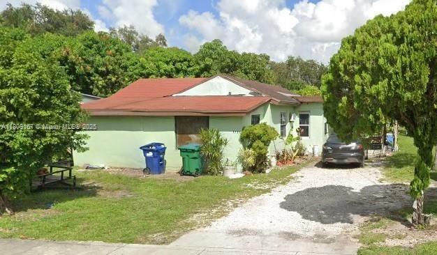 1741 NW 92nd St, Miami, FL 33147 - view of property exterior featuring gravel driveway, stucco siding, and a yard