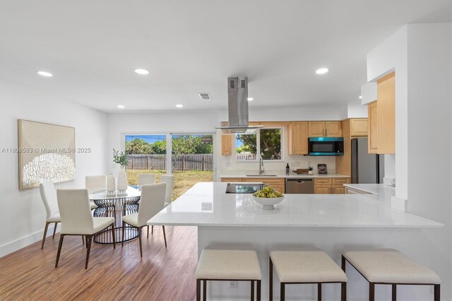 5492 Barnstead Cir, Lake Worth, FL 33463 - kitchen with black appliances, island exhaust hood, a peninsula, a kitchen breakfast bar, and wood finished floors