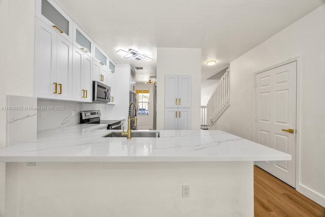 2928 SE 2nd St Unit 5, Homestead, FL 33033 - kitchen with stainless steel appliances, a sink, a peninsula, glass insert cabinets, and light wood-style flooring