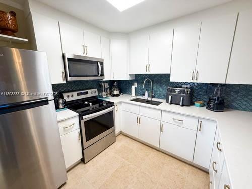 11321 SW 162nd Ter, Miami, FL 33157 - kitchen with appliances with stainless steel finishes, a sink, light countertops, decorative backsplash, and white cabinetry