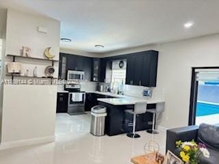 3801 SW 149th Ave, Miami, FL 33185 - kitchen featuring stainless steel electric range oven, dark cabinetry, a peninsula, a kitchen bar, and light countertops