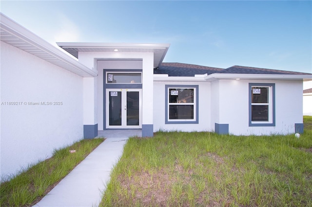 1023 Pilgrim, Lehigh Acres, FL 33974 - view of exterior entry featuring stucco siding, a shingled roof, and a lawn