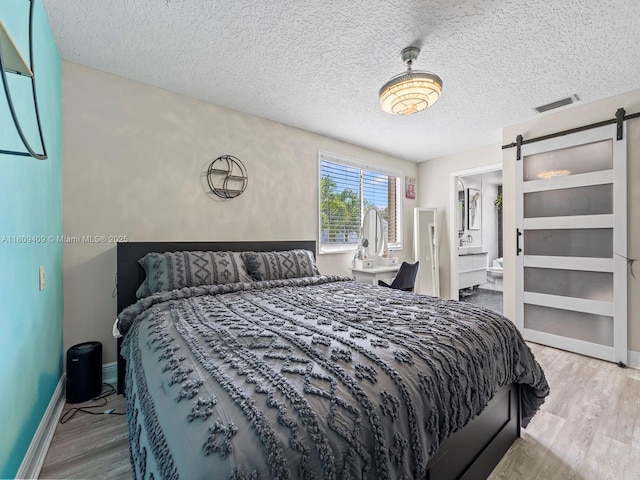 14474 SW 144th Ter, Miami, FL 33186 - bedroom with a barn door, wood finished floors, a textured ceiling, baseboards, and ensuite bath