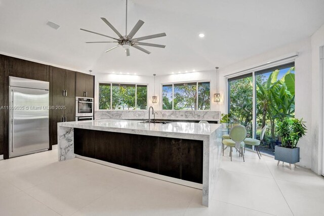 8580 Egret Lakes Ln, West Palm Beach, FL 33412 - kitchen featuring built in refrigerator, a spacious island, dark brown cabinets, light stone counters, and ceiling fan