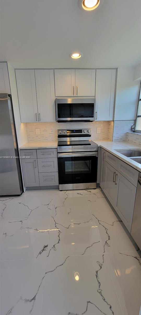 2301 NW 41st Ave Unit 209, Lauderhill, FL 33313 - kitchen with stainless steel appliances, light marble finish flooring, gray cabinetry, backsplash, and recessed lighting
