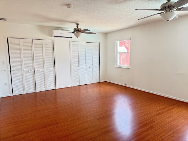 6561 W 13th Ct, Hialeah, FL 33012 - unfurnished bedroom with two closets, wood finished floors, a wall mounted air conditioner, a textured ceiling, and baseboards