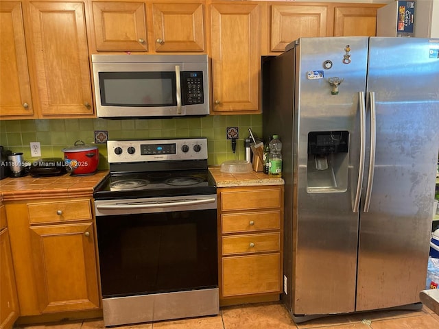 1770 NE 191st St Unit 316-1, Miami, FL 33179 - kitchen featuring stainless steel appliances, tile countertops, backsplash, and brown cabinets